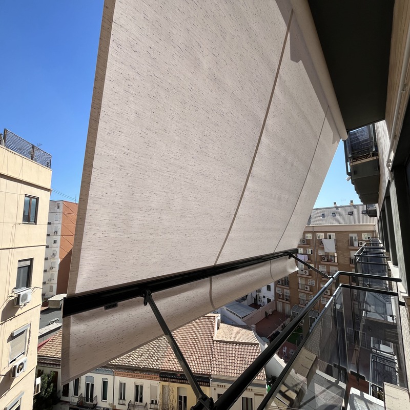 Toldo punto recto en una fachada con ventana y balcón